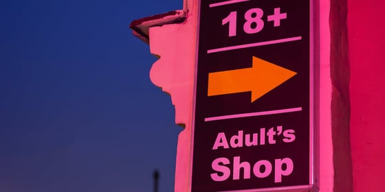 Sign with an arrow pointing toward an adult store using commercial real estate loans, where shoppers must be 18 years or older to enter