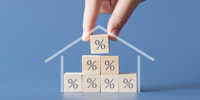 Hand placing percentage blocks inside a house, representing the connection between interest rates and private investments