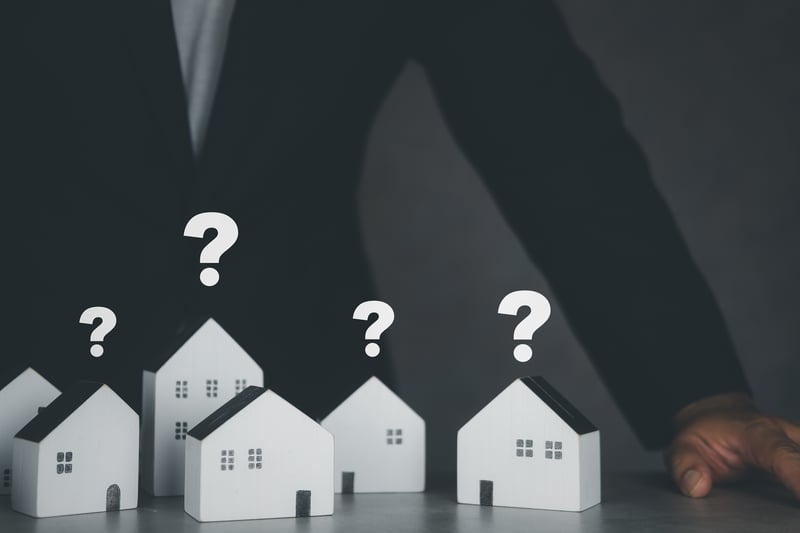 Paper houses with question marks over them and man with questions about hard money loans